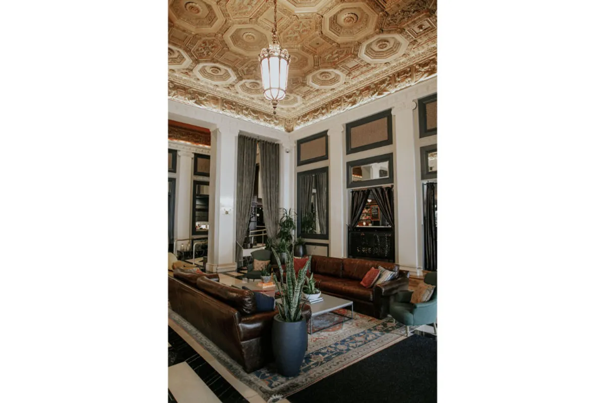 A sophisticated lounge with ornate ceiling details, leather couches, indoor plants, and a striking light fixture. The setting is comfortable yet elegant, ideal for relaxing, reconnecting, and enjoying downtime together.