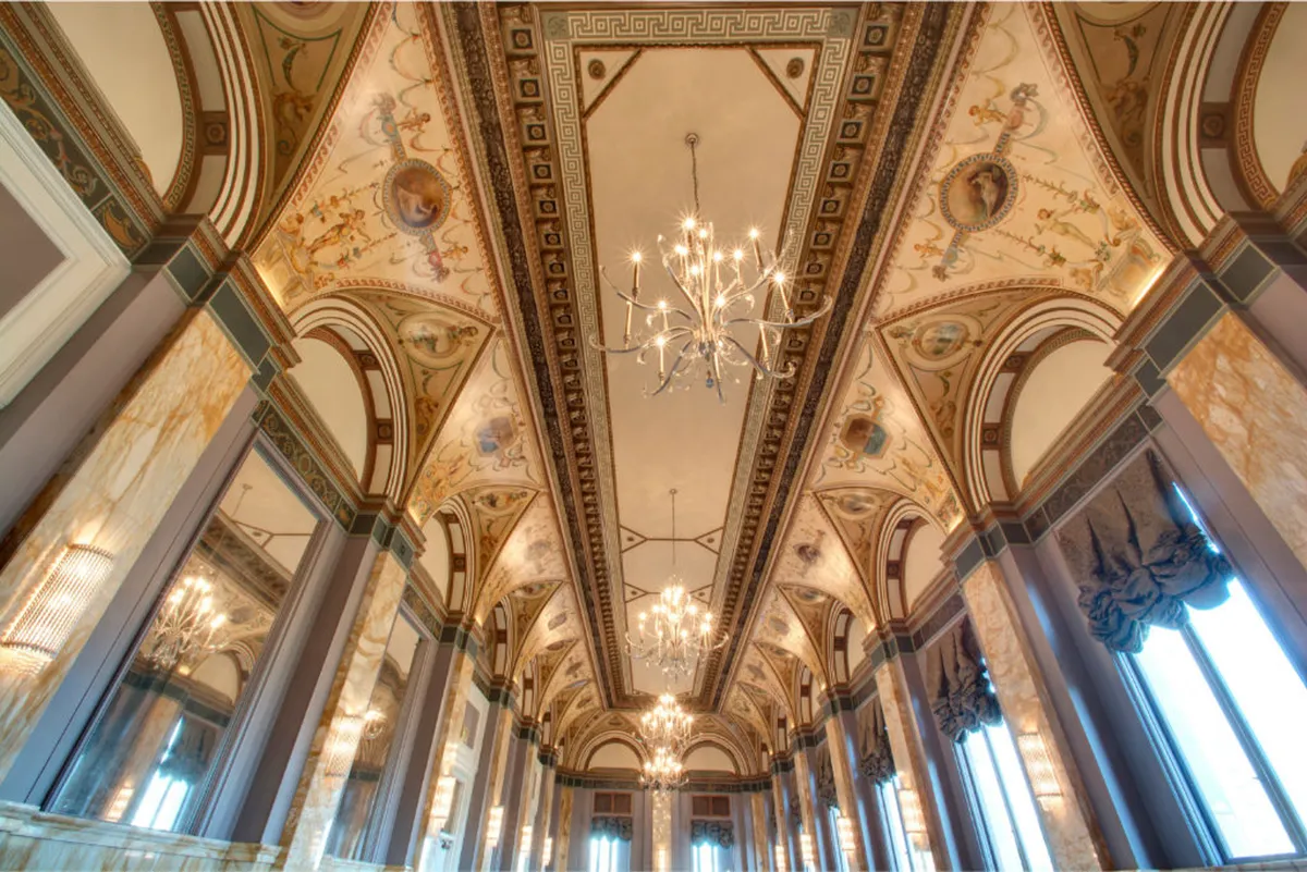 A beautifully appointed lobby with an ornate ceiling, sparkling chandeliers, marble columns, and decorative walls. The atmosphere is both elegant and inviting—ideal for romantic arrivals, social gatherings, and sophisticated wine hours.