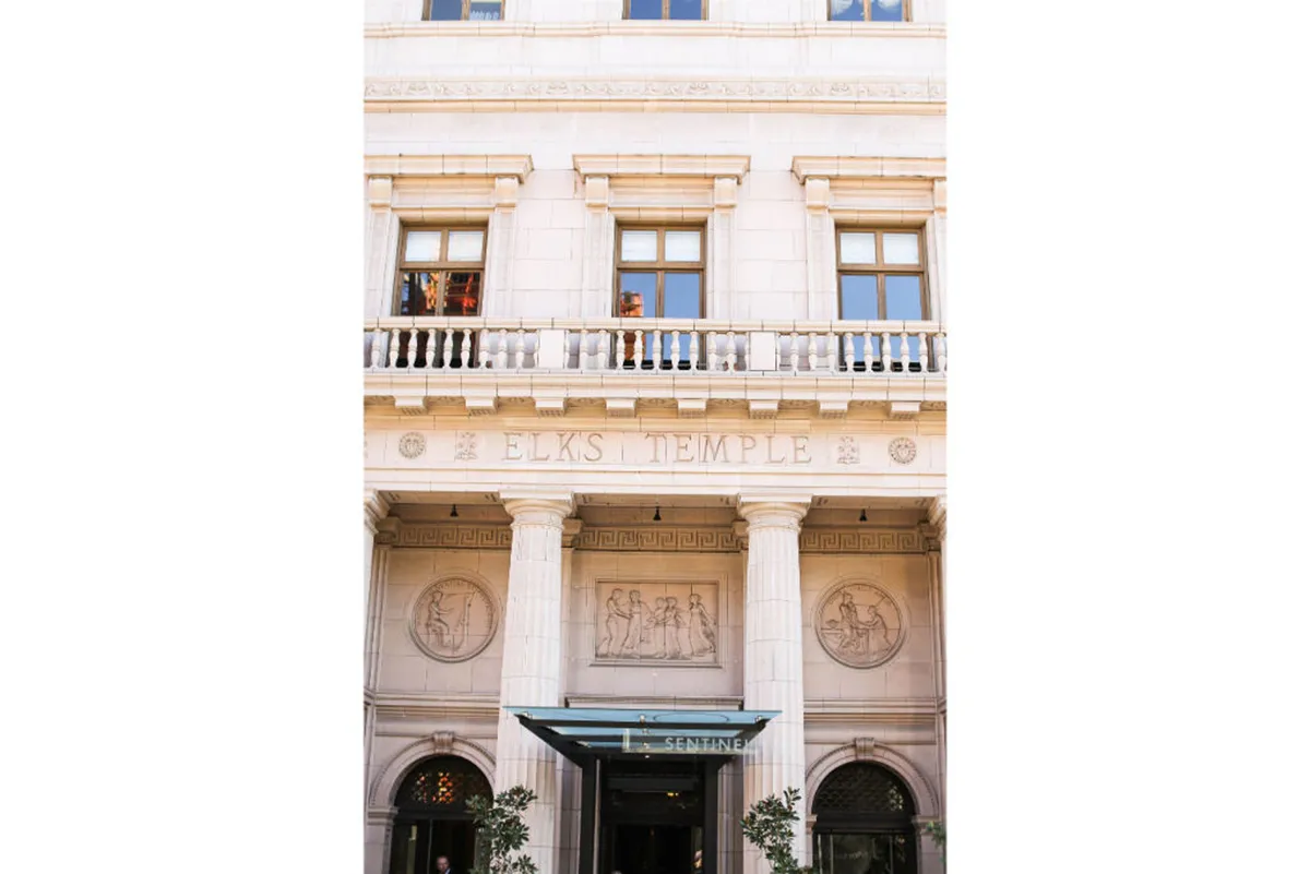 An elegant exterior view of the Hotel Sentinel, featuring its distinguished architectural details, a prominent entrance awning, and an engraved stone facade. The scene sets a sophisticated tone, suggesting a grand arrival experience and hinting at the luxury within.