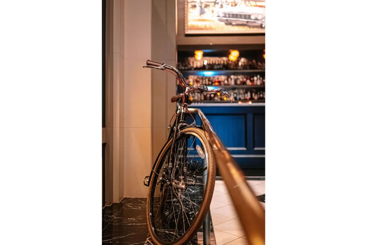 A casual, inviting interior scene featuring a bicycle positioned near a stylish bar area, complemented by modern lighting fixtures. The setting conveys a relaxed atmosphere perfect for spontaneous meet-ups or unwinding after a day in the city.