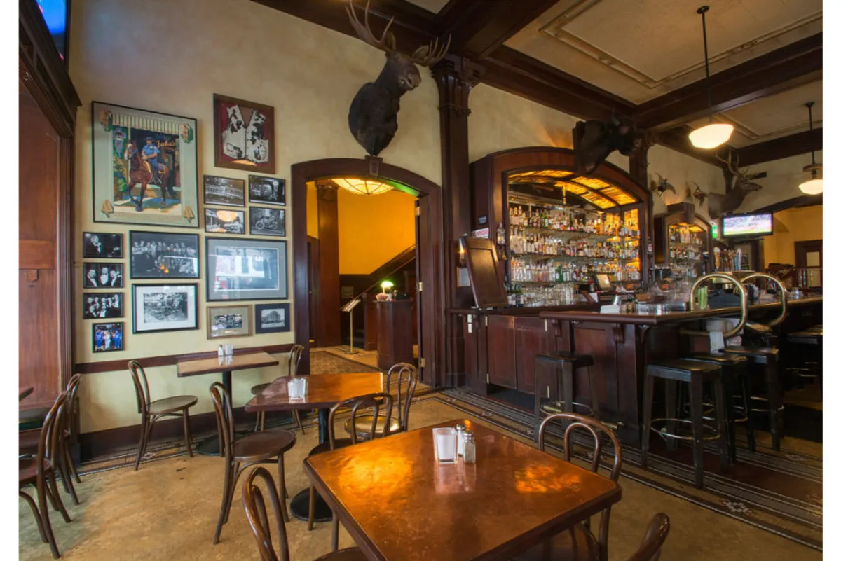 A cozy bar with wooden tables, characterful décor including moose heads, and photographs on the wall. The ambiance is relaxed and informal, with guests enjoying drinks and conversation in a space full of personality and local charm.