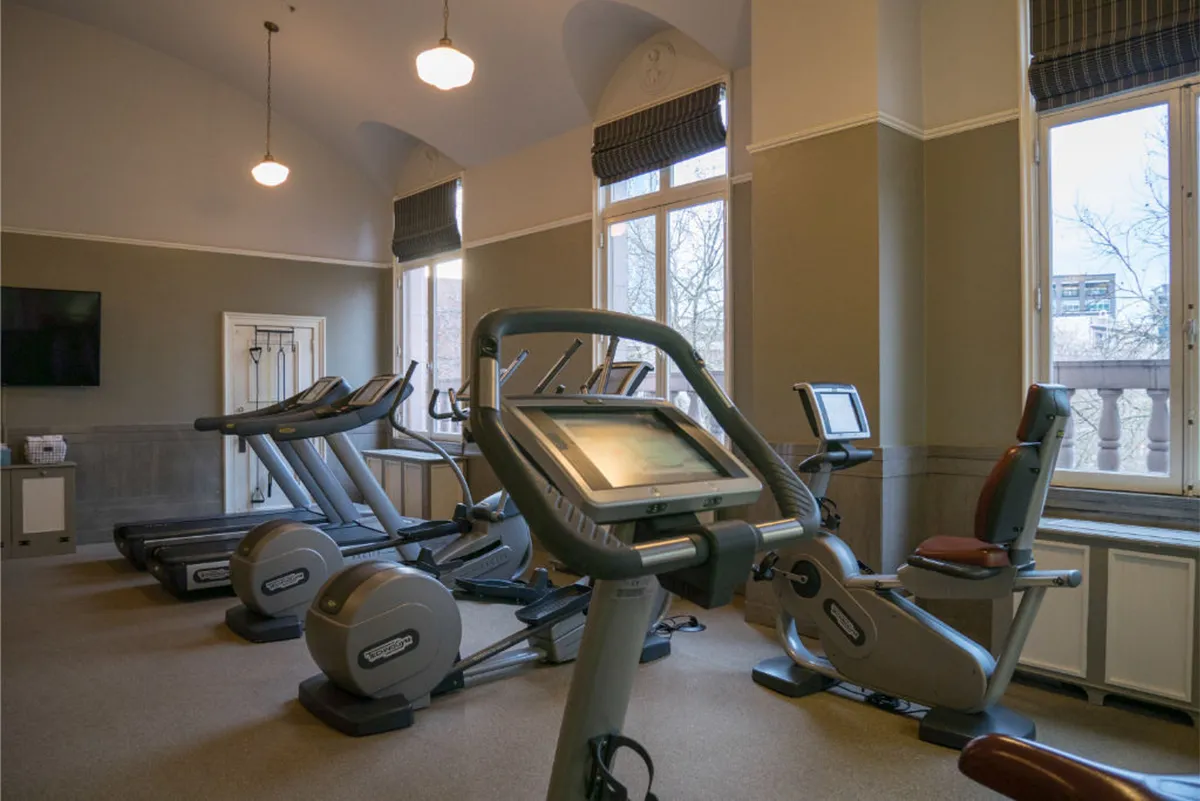 A bright, modern fitness center filled with state-of-the-art exercise machines, large windows letting in abundant natural light, and a wall-mounted TV for entertainment. The space is clean and inviting, ideal for guests wanting to maintain their wellness routines.