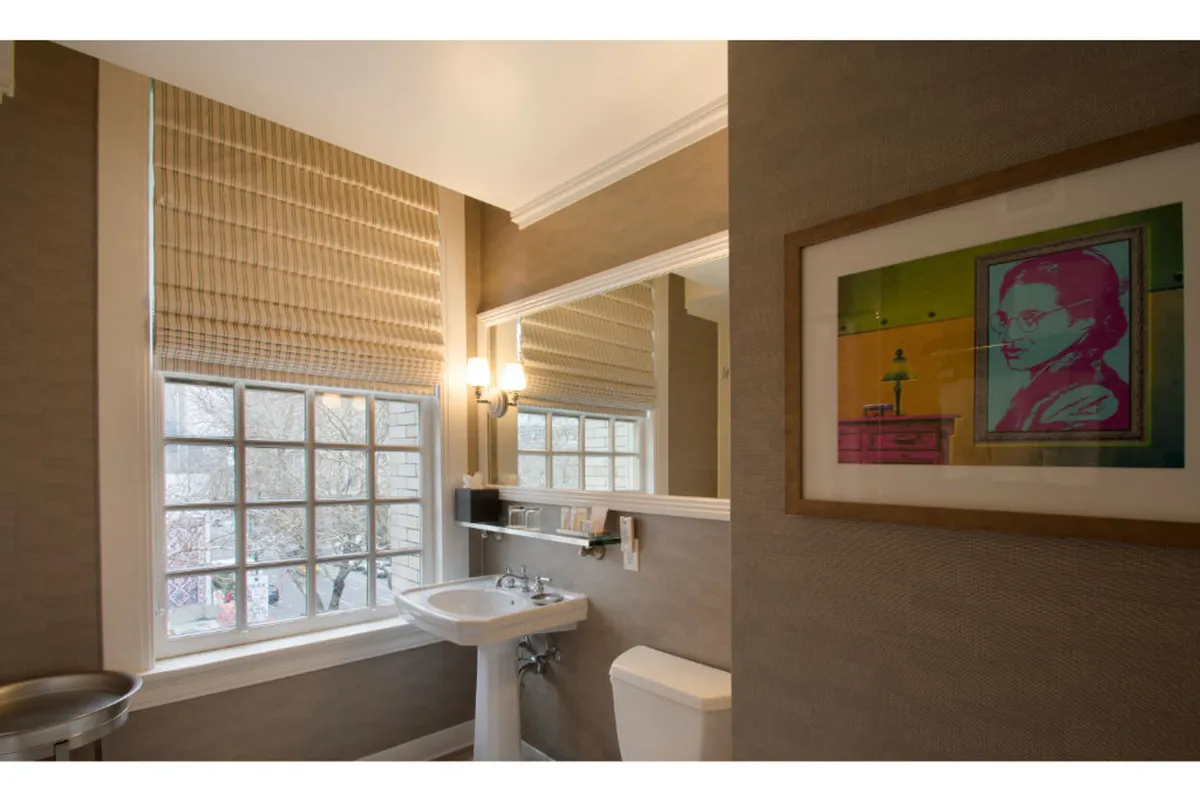 A contemporary bathroom with a sleek sink and mirror, accented by curated artwork and a window that lets in ample daylight. The overall feel is stylish and artistic, with a strong emphasis on both utility and aesthetics.