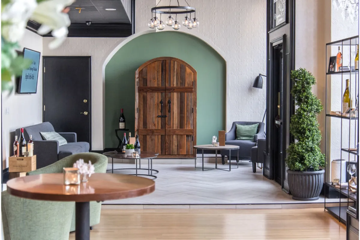 A cozy, stylish interior with a wooden door, a calming green wall, comfortable seating, and an elegant wine display. The ambiance suggests relaxation and comfort, enhanced by thoughtful design details.